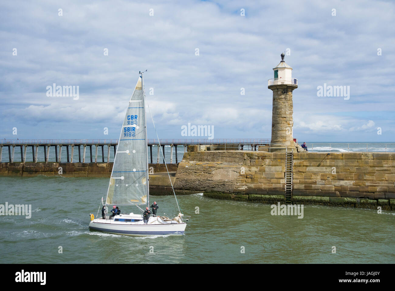 Whitby, North Yorkshire, England. VEREINIGTES KÖNIGREICH. Yacht-segeln in den Hafen, vorbei an Leuchtturm und piers Stockfoto