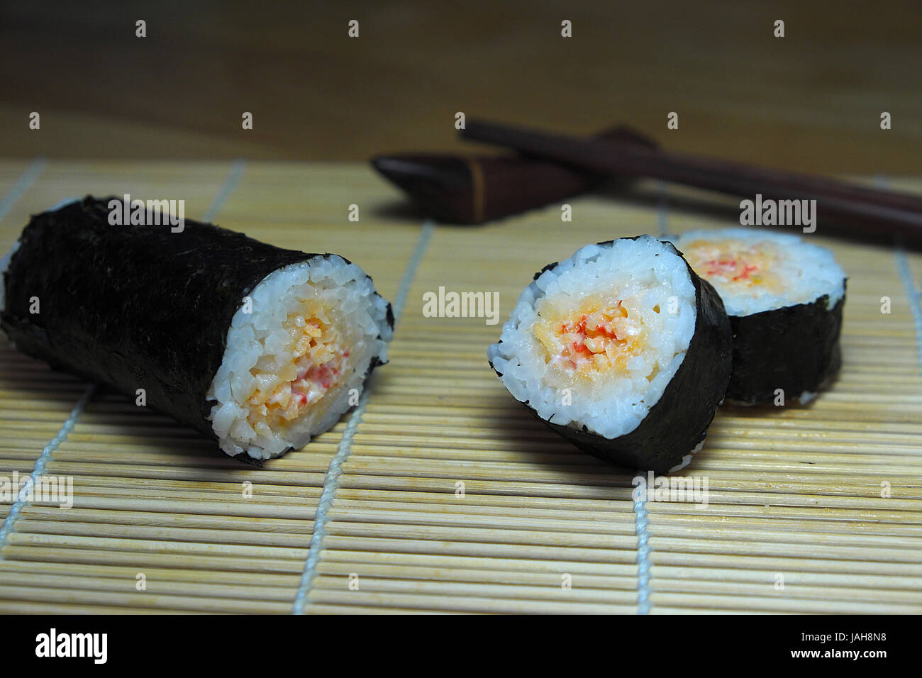 Sushi-Rollen mit Stäbchen, auf hölzernen Bambusmatte auf Algen. Stockfoto