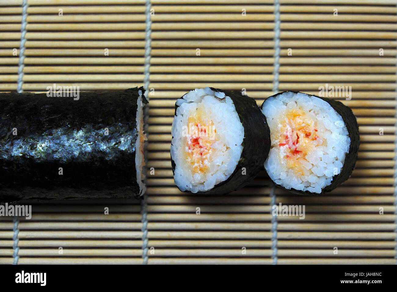 Sushi-Rollen mit Stäbchen, auf hölzernen Bambusmatte auf Algen. Ansicht von oben. Stockfoto