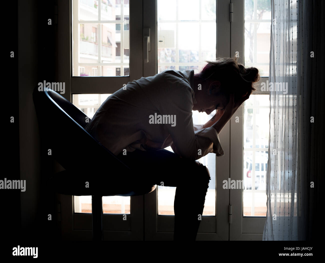 Junge leidenden Frau weinend zu Hause Hintergrundbeleuchtung Hände über Kopf Stockfoto