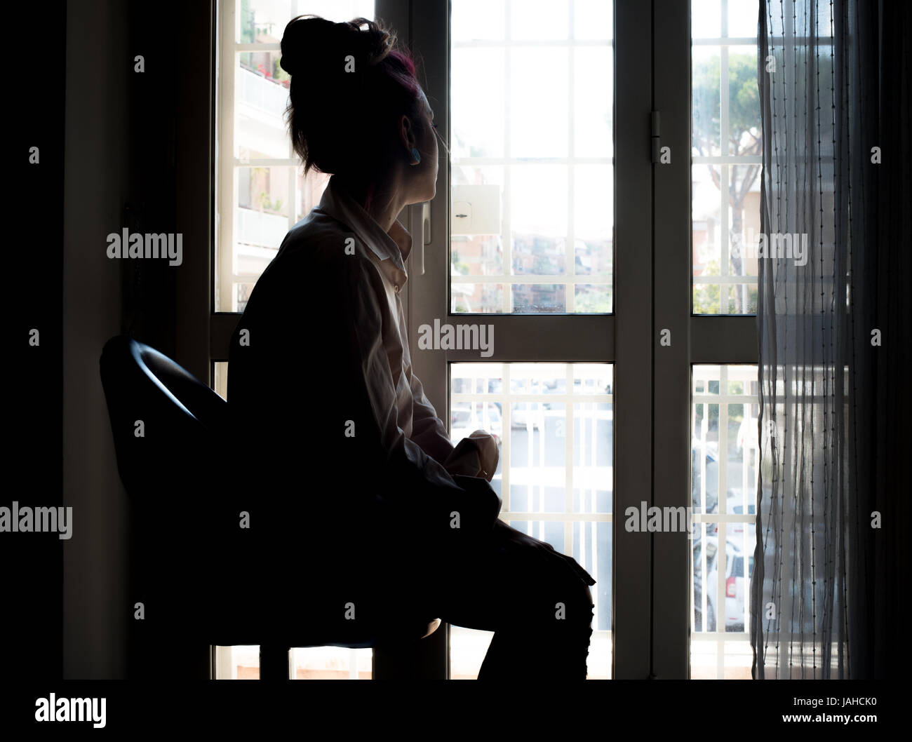 Junge nachdenkliche, traurige Frau Blick aus Fenster zu Hause Hintergrundbeleuchtung Stockfoto