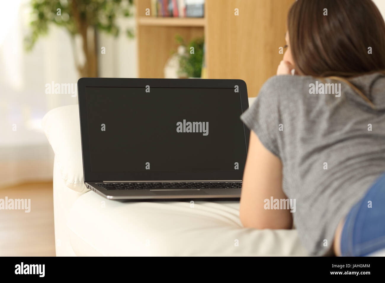 Rückansicht eines Mädchens beobachten Medieninhalte in einem Laptop zeigt einen leeren Bildschirm auf einer Couch im Wohnzimmer zu Hause Stockfoto