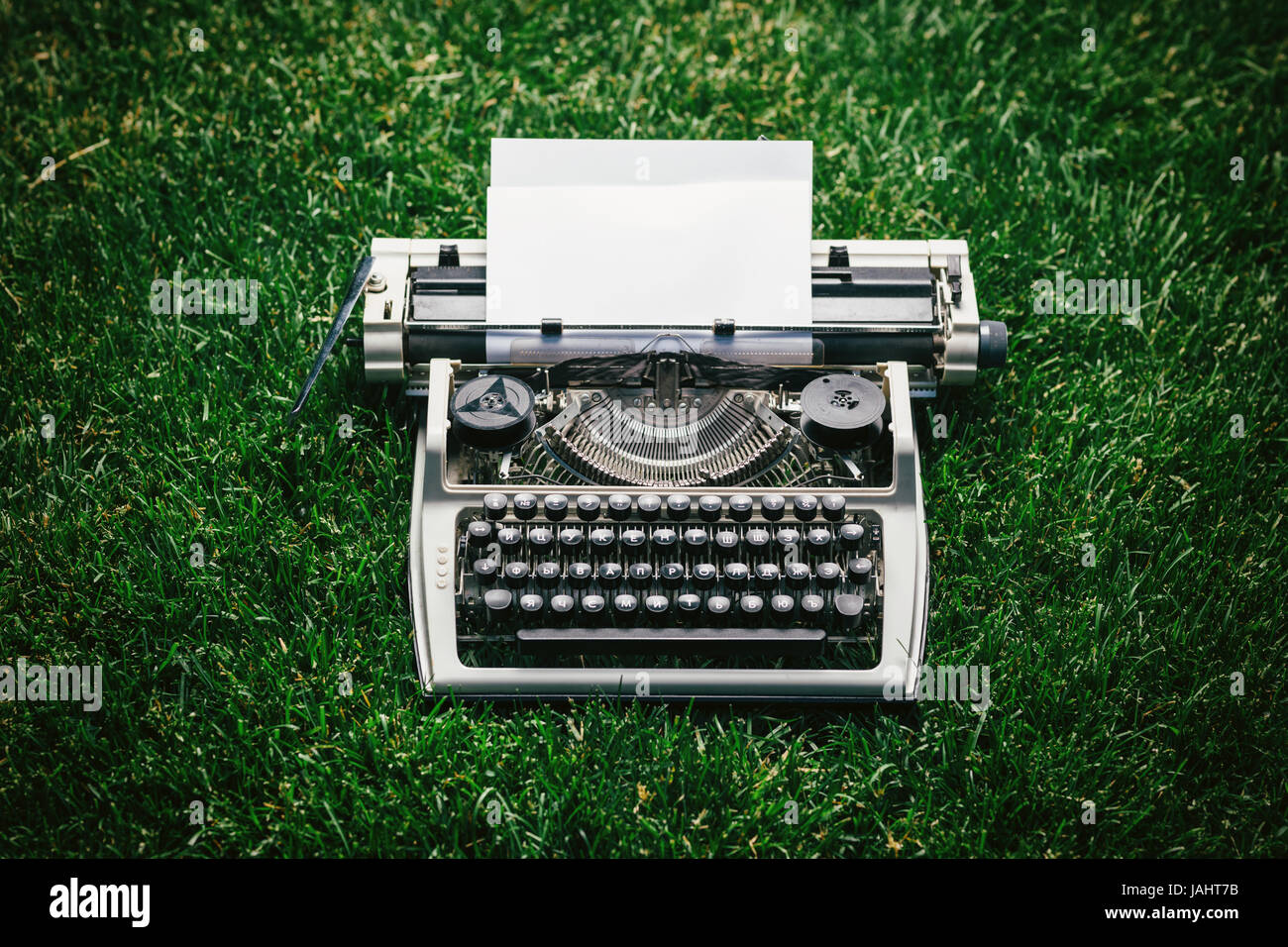Foto von alten Schreibmaschine auf dem grünen Rasen mit einem Blatt Papier. Stockfoto