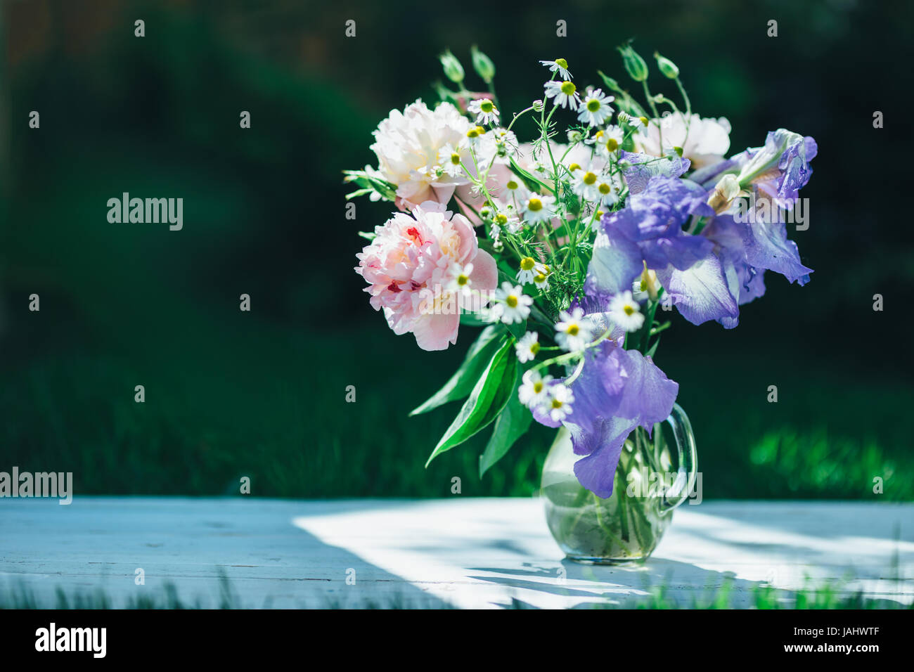 Bouquet von weißen Pfingstrosen, Kamillen und Iris Blumen in Glasvase. Sommer Hintergrund. Getönte Foto Stockfoto