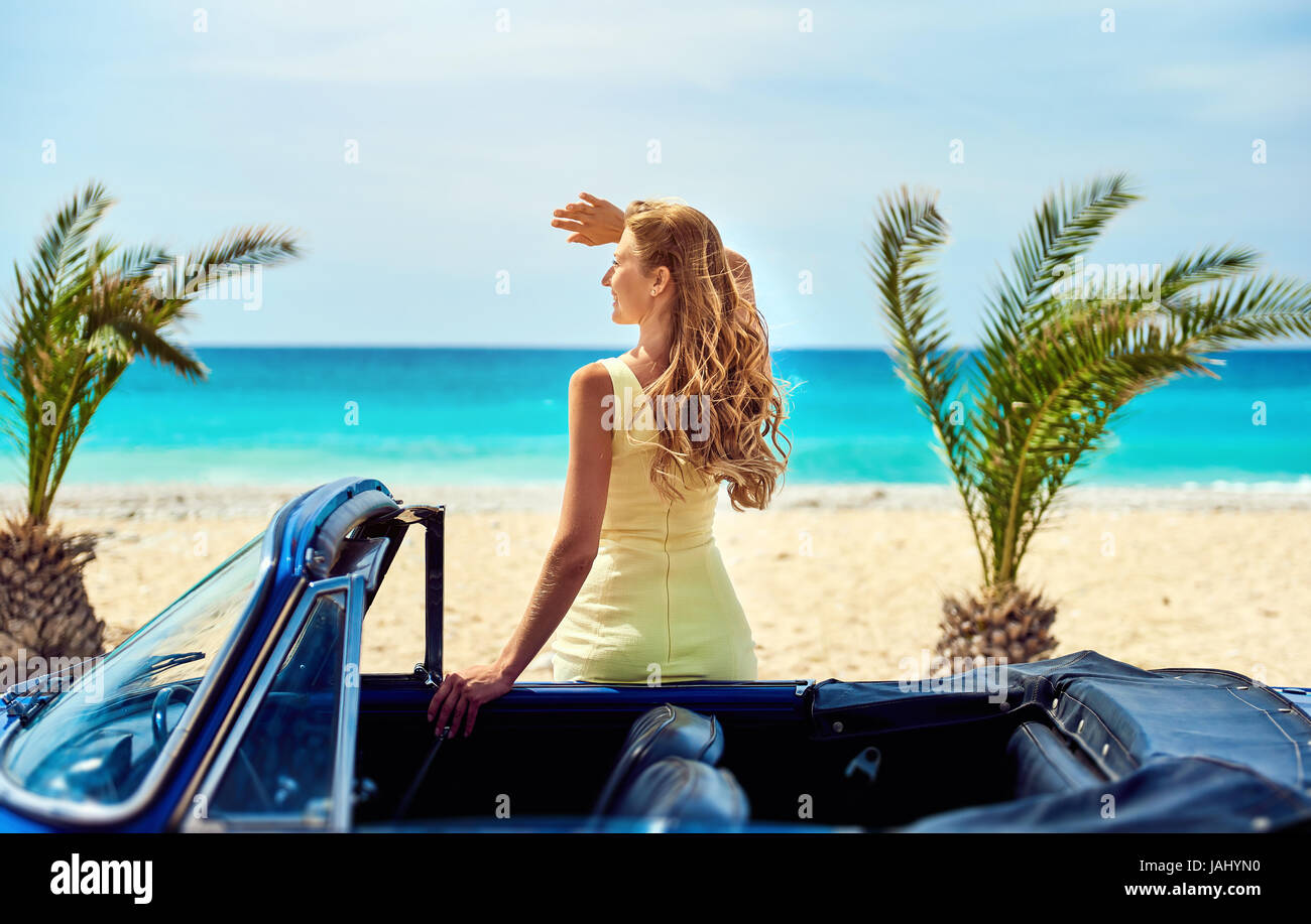 Attraktive Frau in der Nähe von Retro-Auto am tropischen Strand. Türkisfarbenen Meer. Idyllische Landschaft Stockfoto