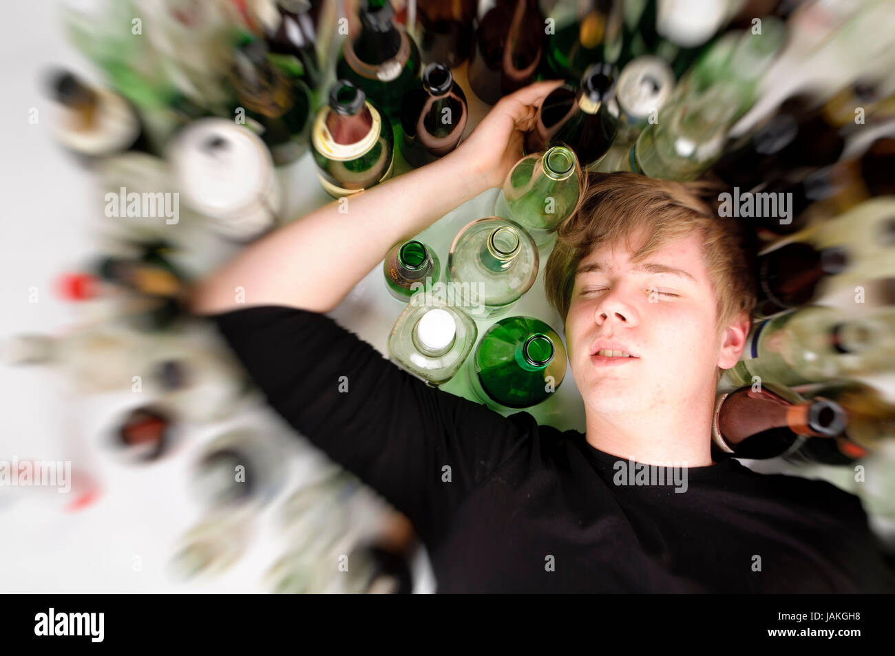 Junger Mann Mit 100-jähriges blonden Haaren Liegt Auf Dem Boden Und ist von Vielen enthalten Bier-Und Schnapfsflaschen diesen, Oberperspektive. Stockfoto