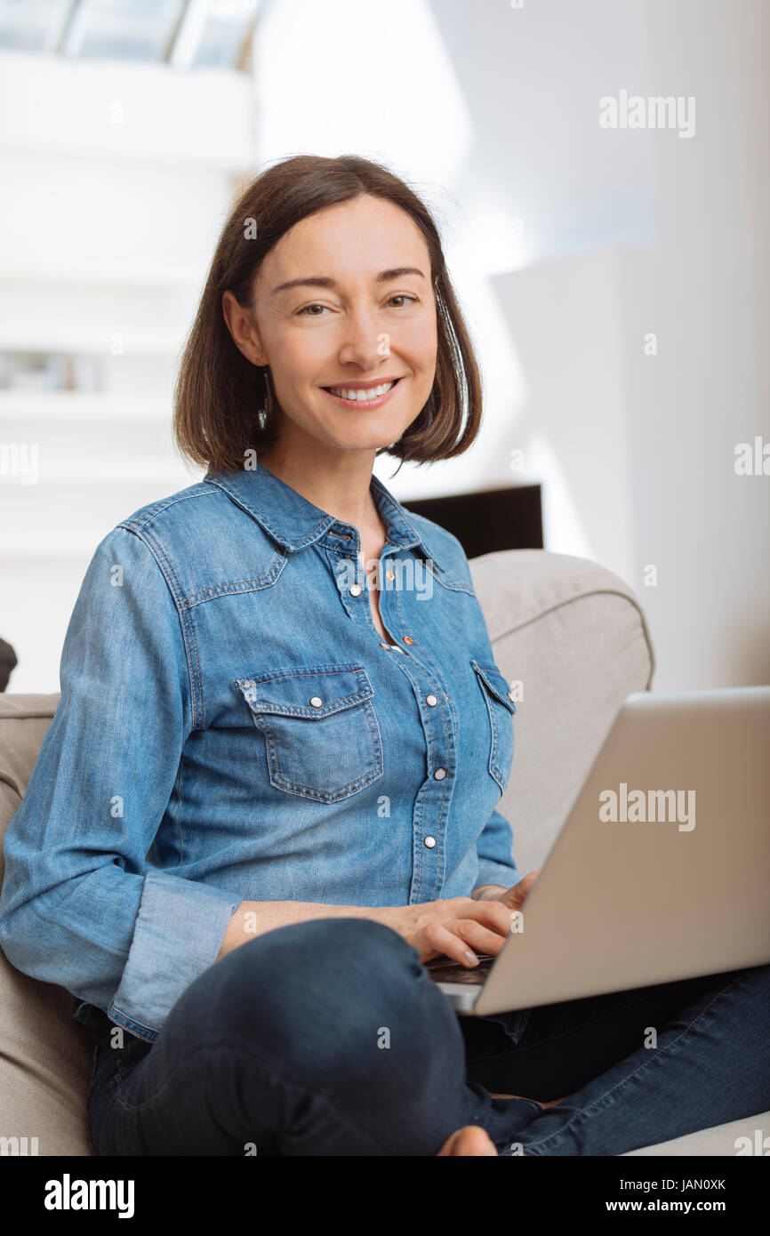 Attraktive Reife Frau mit einem Laptop während Sie gemütlich auf dem Sofa zu Hause Stockfoto