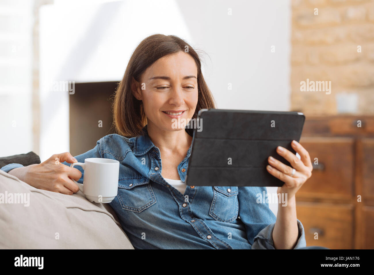 Reife Frau mit Tablet-PC, während Sie gemütlich auf dem Sofa zu Hause Stockfoto