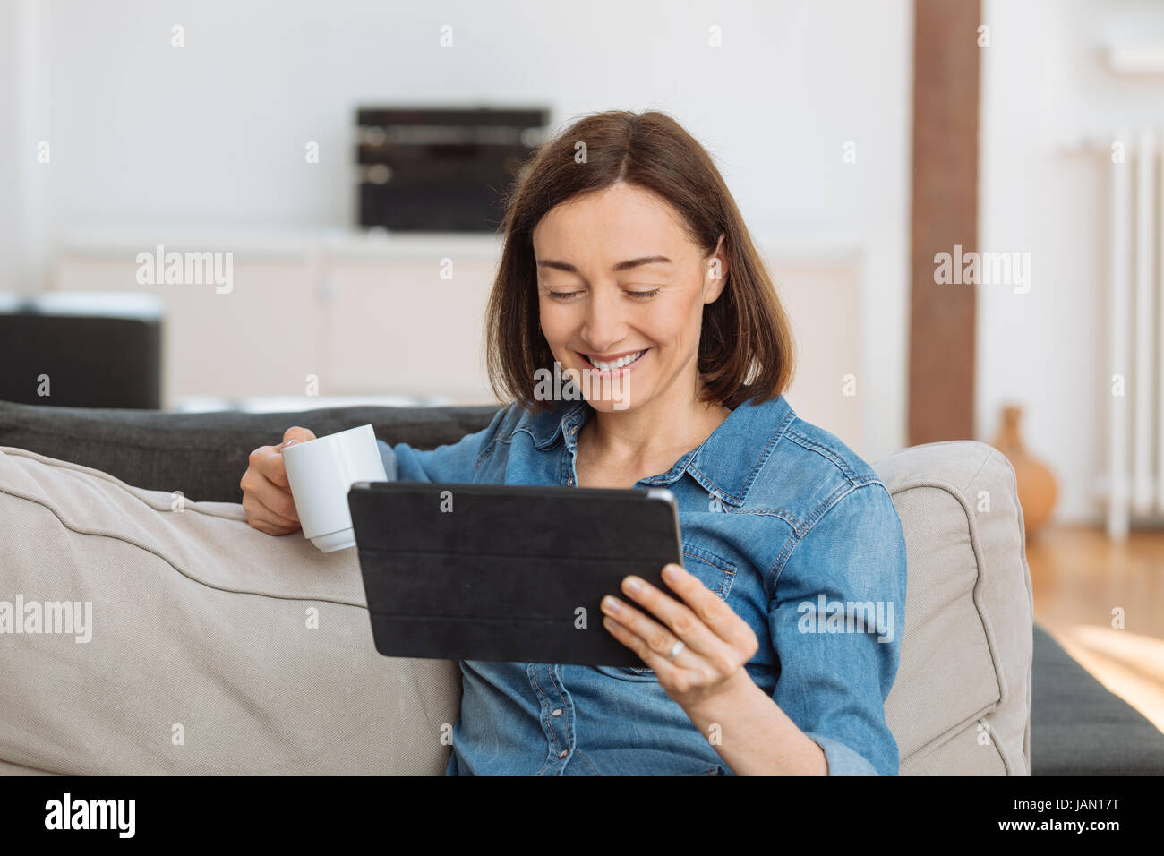 Reife Frau mit Tablet-PC, während Sie gemütlich auf dem Sofa zu Hause Stockfoto