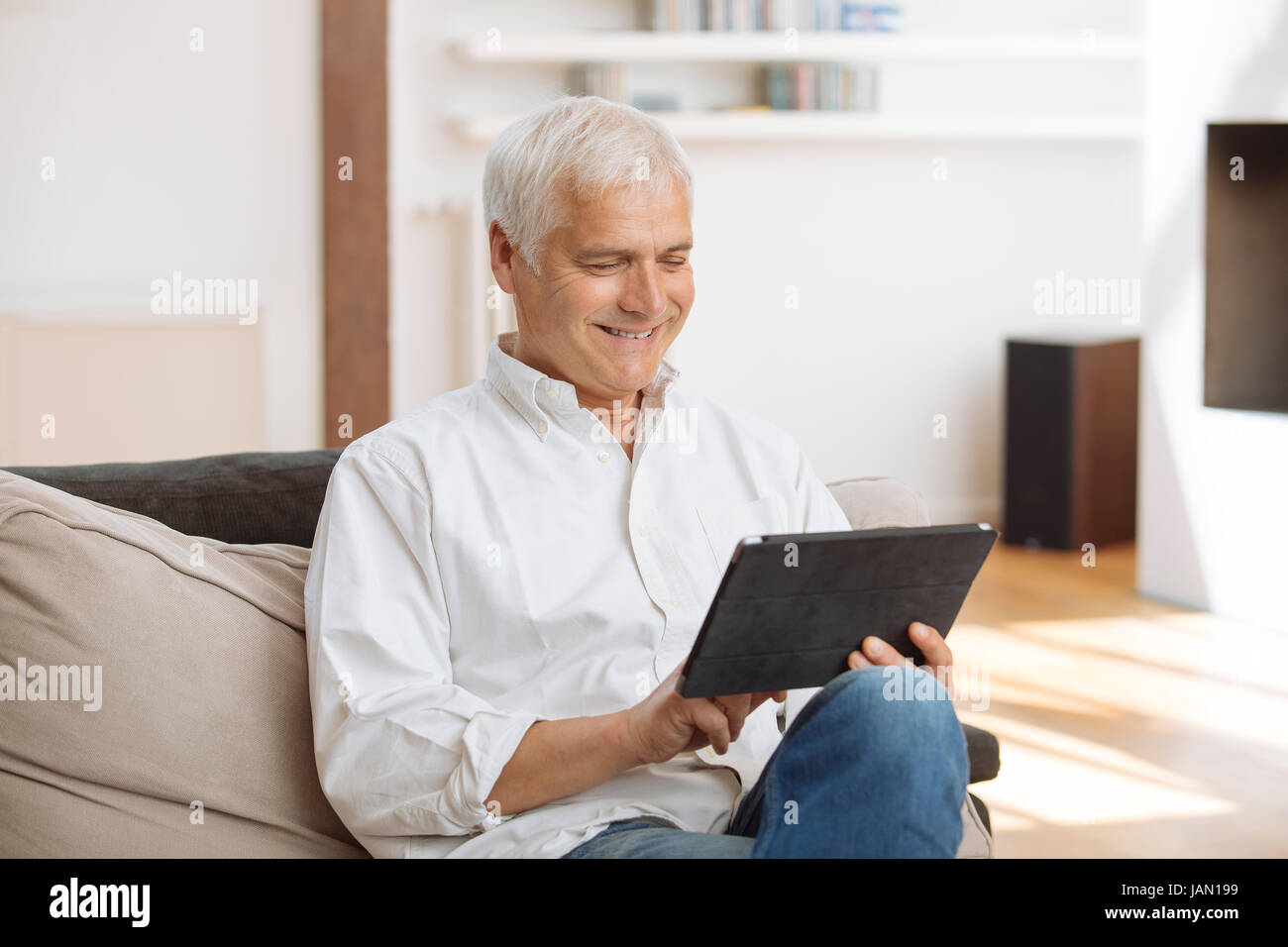 Lächelnd reifen Mann sitzt auf einem Sofa mit einem TabletPC im Wohnzimmer Stockfoto