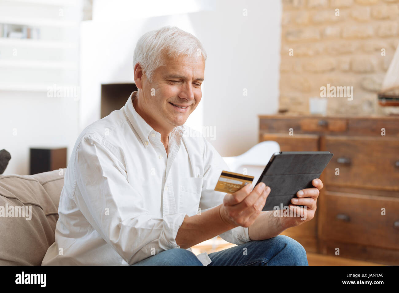 reifer Mann mit seinem Laptop und hält seine Kreditkarte Stockfoto