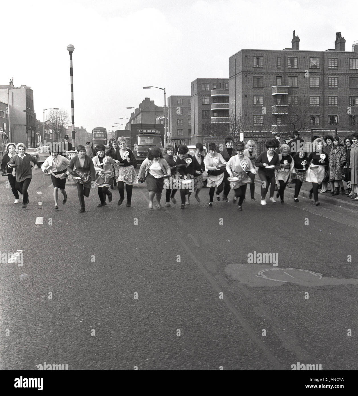1965, old Kent Road, Peckham, London und eine Gruppe von Damen auf den Weg in ihre Schürzen und Pfannen für das Traditionsrennen Faschingsdienstag Panacke tragen. Stockfoto