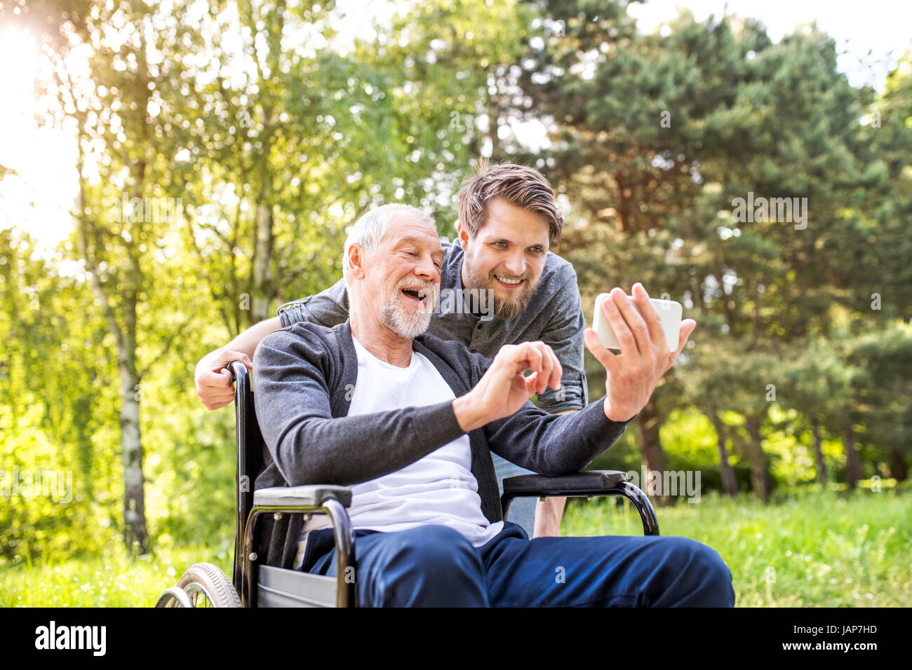 Hipster-Sohn und Vater im Rollstuhl im Park nehmen Selfie. Stockfoto
