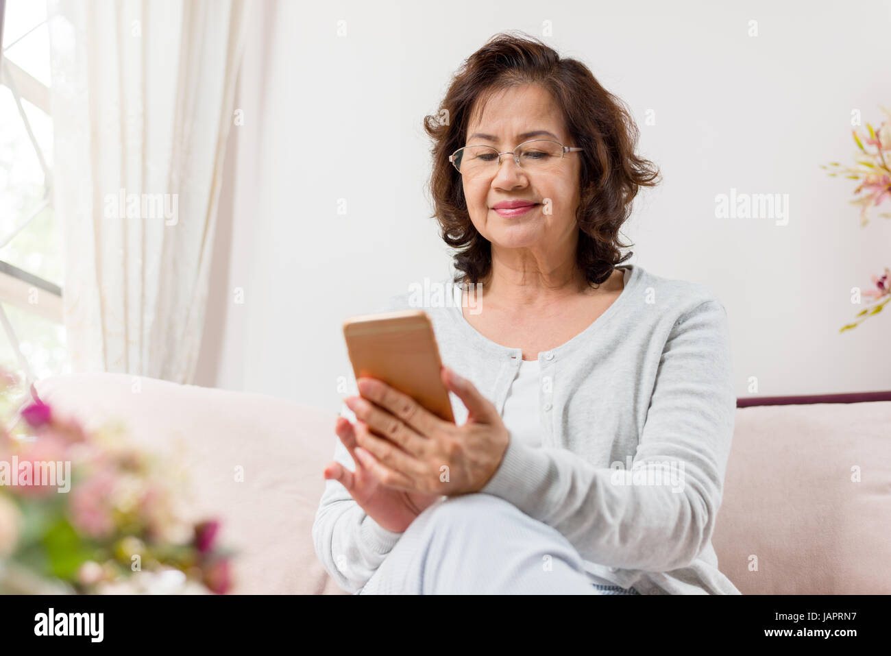 Glücklich senior Asiatin auf Sofa sitzen und mit einem smart-phone Stockfoto