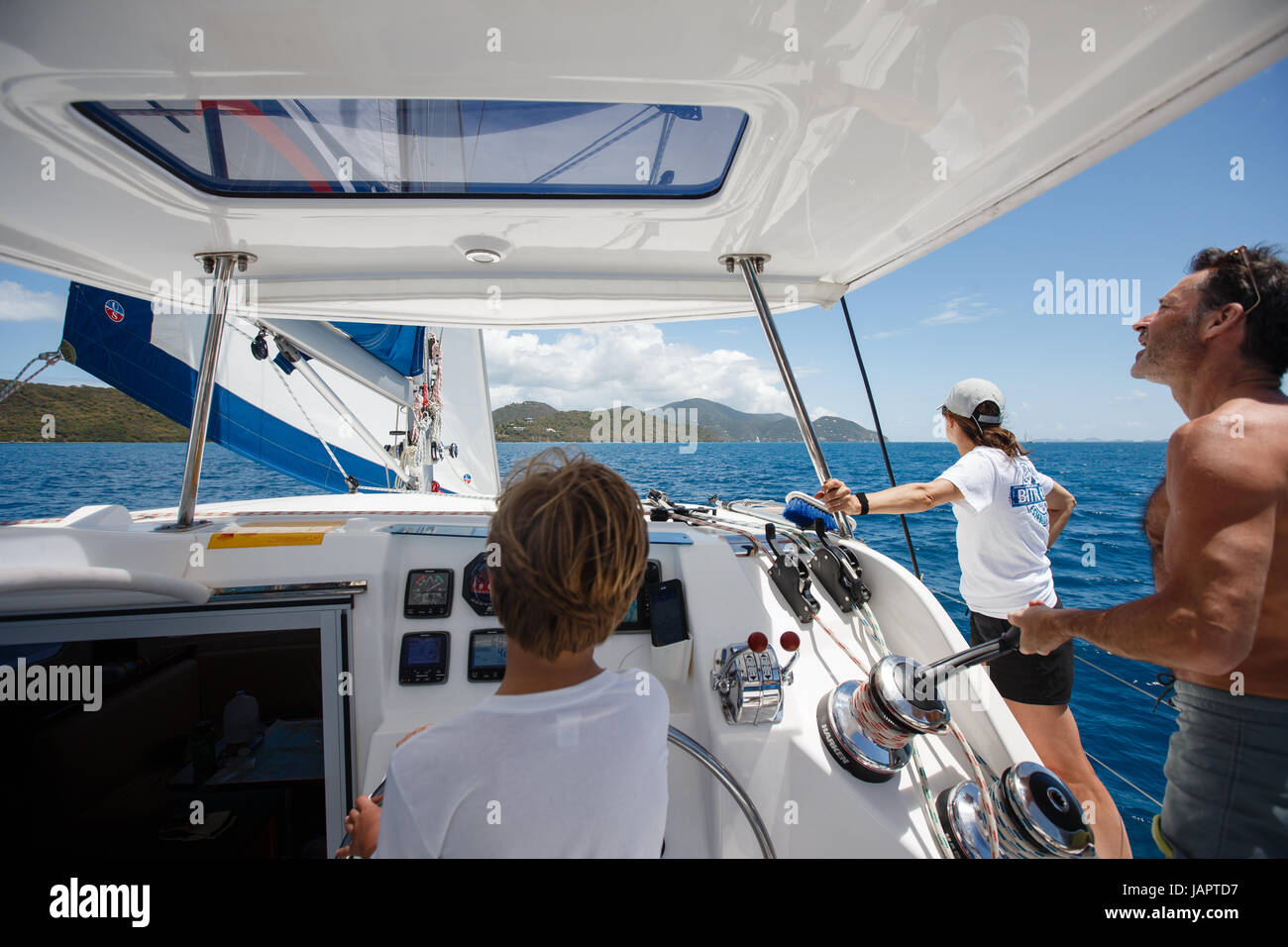 ein kleiner Junge am Ruder Segeln Katamaran in das türkisfarbene Wasser des karibischen Meeres aus den British Virgin islands Stockfoto