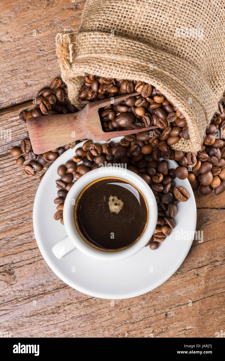 rustikale Tasche voller Kaffeebohnen mit Holz- und Tasse Kaffee auf Holztisch Stockfoto