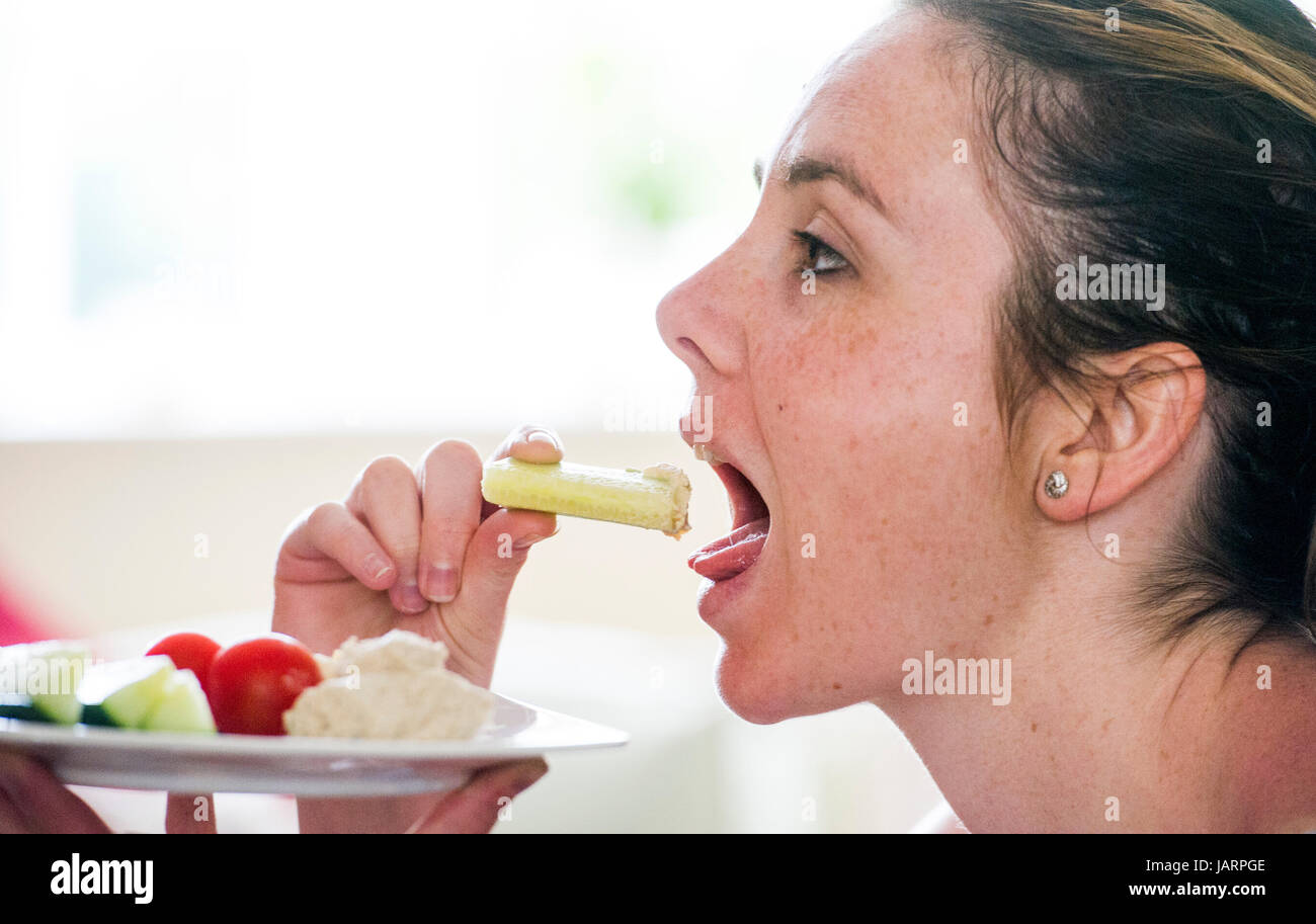 Junge Frau in ihren 20ern gesunder Ernährung Gurke mit humosen Hummus oder Hommous hergestellt aus gekochten Kichererbsen Knoblauch, Gewürze, Tahin, Olivenöl und Stockfoto