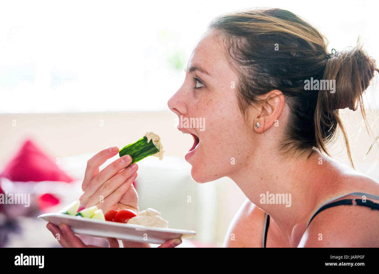 Junge Frau in ihren 20ern gesunder Ernährung Gurke mit humosen Hummus oder Hommous hergestellt aus gekochten Kichererbsen Knoblauch, Gewürze, Tahin, Olivenöl und Stockfoto