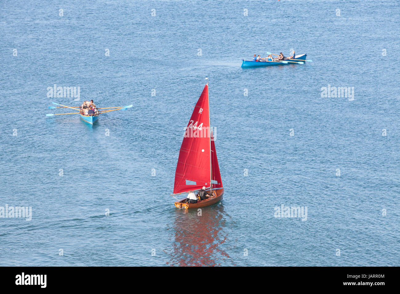 Eine Jolle mit einem roten Segel und zwei Piloten Gigs ab Looe, Cornwall Stockfoto