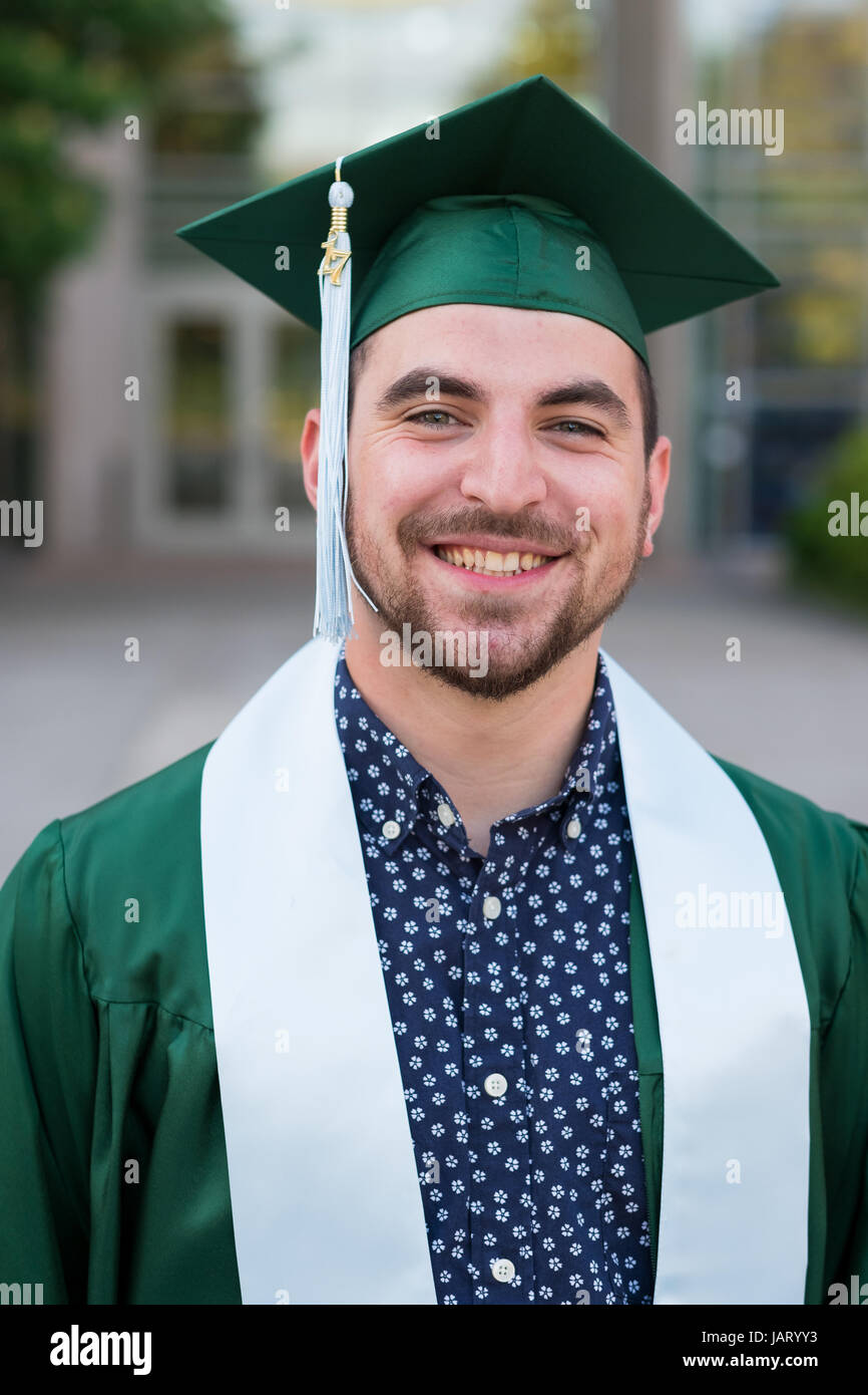 College Senior stellt für eine Abschlussfeier Foto auf dem Campus in seiner Kappe und Kleid. Stockfoto