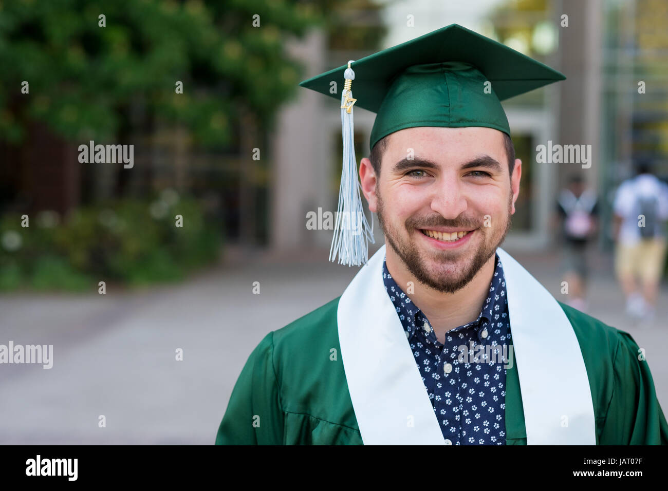 College Senior stellt für eine Abschlussfeier Foto auf dem Campus in seiner Kappe und Kleid. Stockfoto