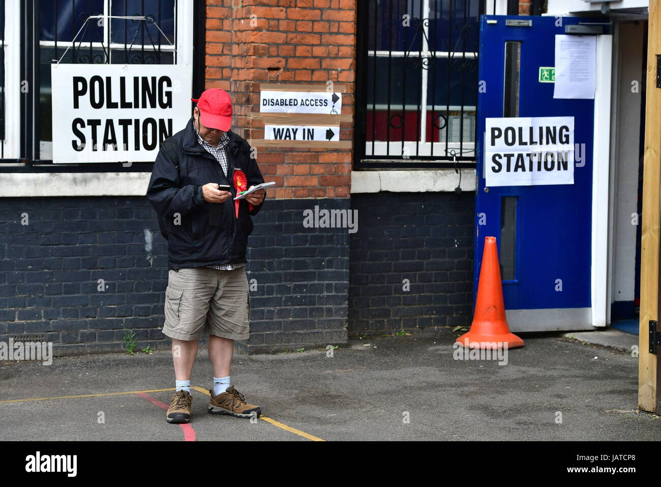 Ein Mann trägt eine Arbeiterpartei Rosette steht er vor dem Wahllokal an der Pakeman School in Islington, North London, wo Labour-Chef Jeremy Corbyn seine Stimme bei den allgemeinen Wahlen werfen wird. Stockfoto