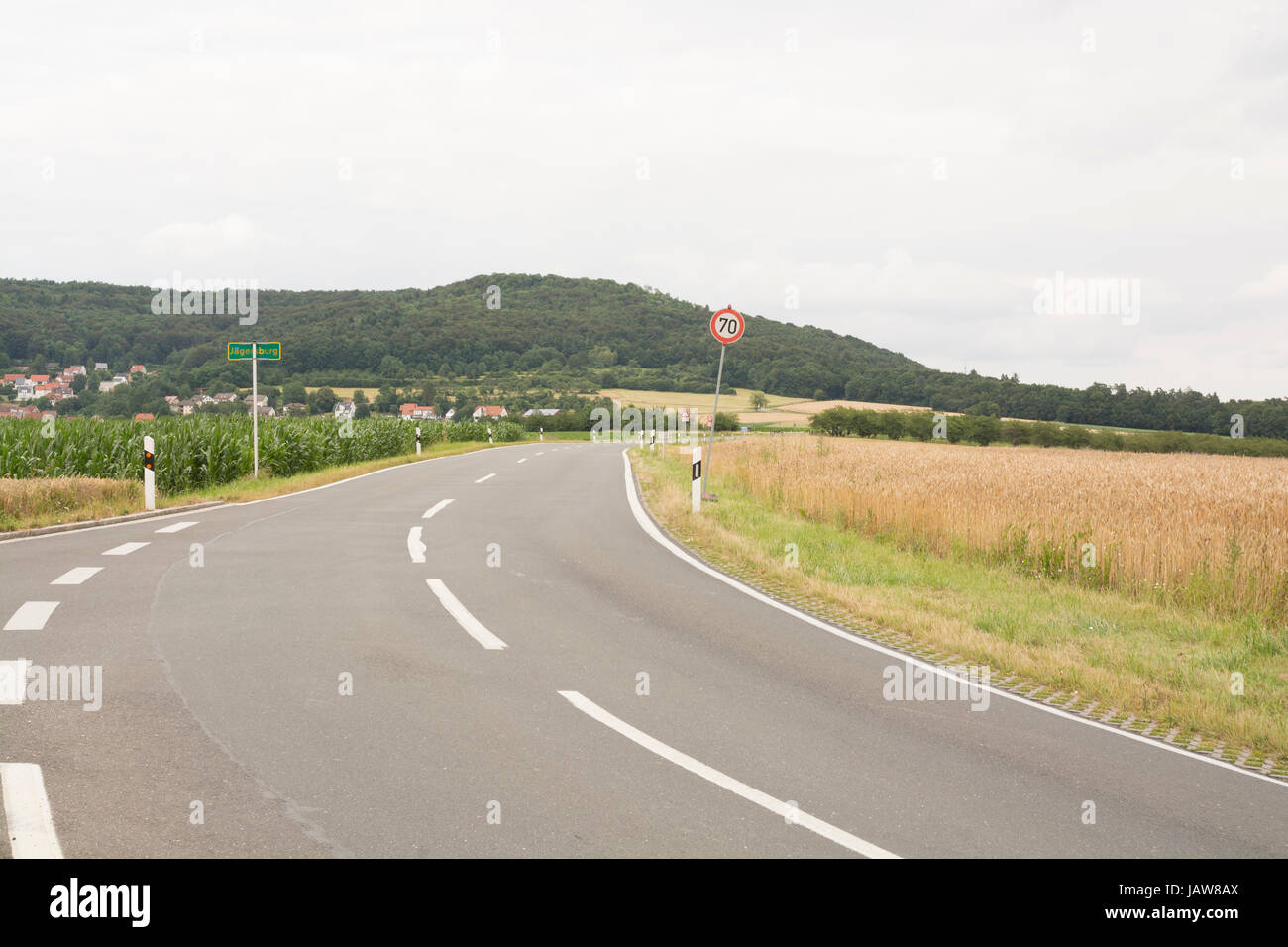 Straße entlang einem Weizenfeld in Bayern, Deutschland - grüne Hügel, goldene Weizenfeld und sauberer Straßenfahrzeuge. Weizenfeld in Bayern, Deutschland - goldene Zeit Ansätze Stockfoto