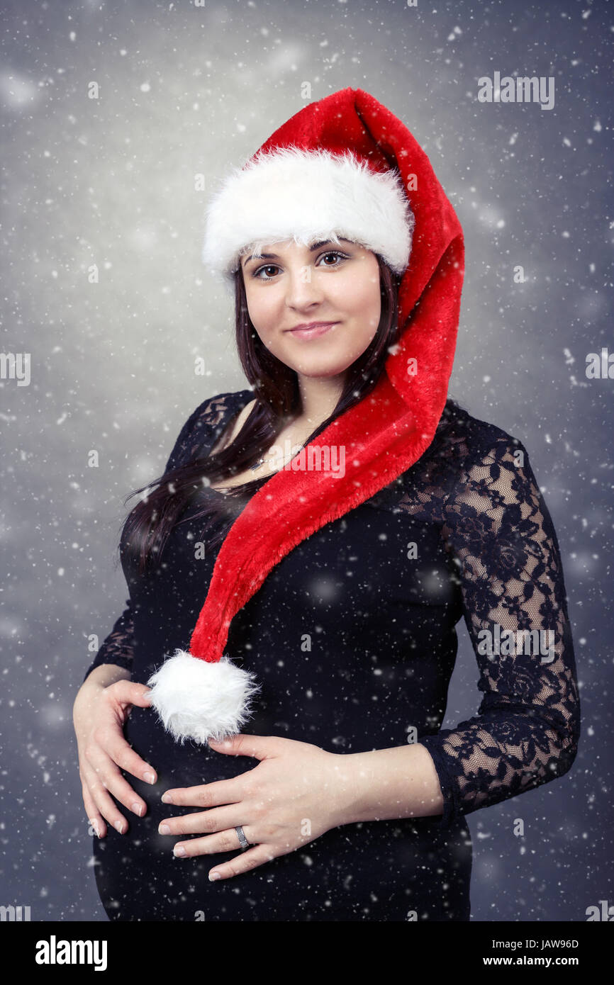 schönen lächelnden jungen Santa schwangere zärtlich hält ihren Bauch mit schneit im Hintergrund Stockfoto