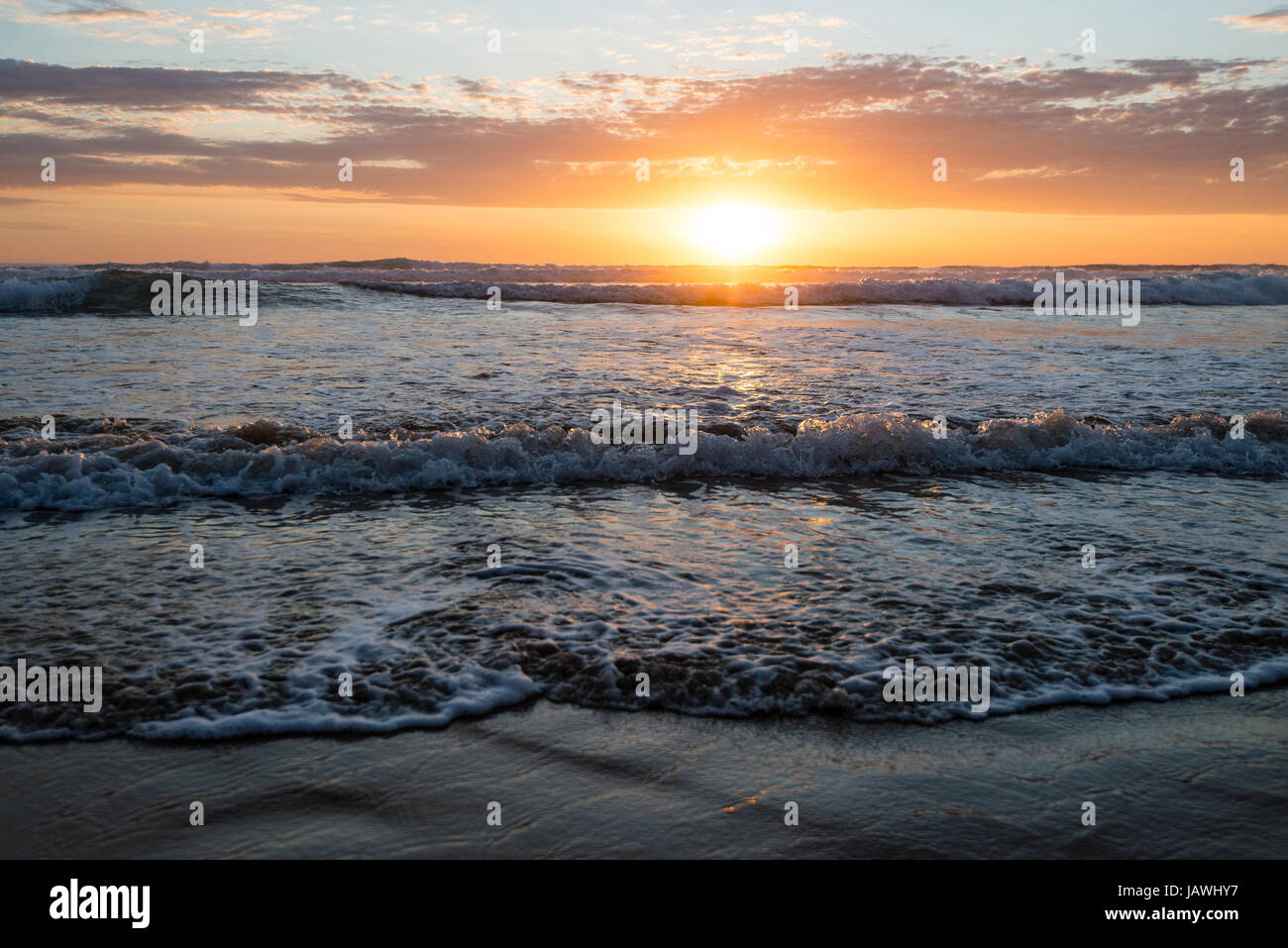 Eine Flut schiebt Wellen auf einen Strand bei Sonnenuntergang. Stockfoto