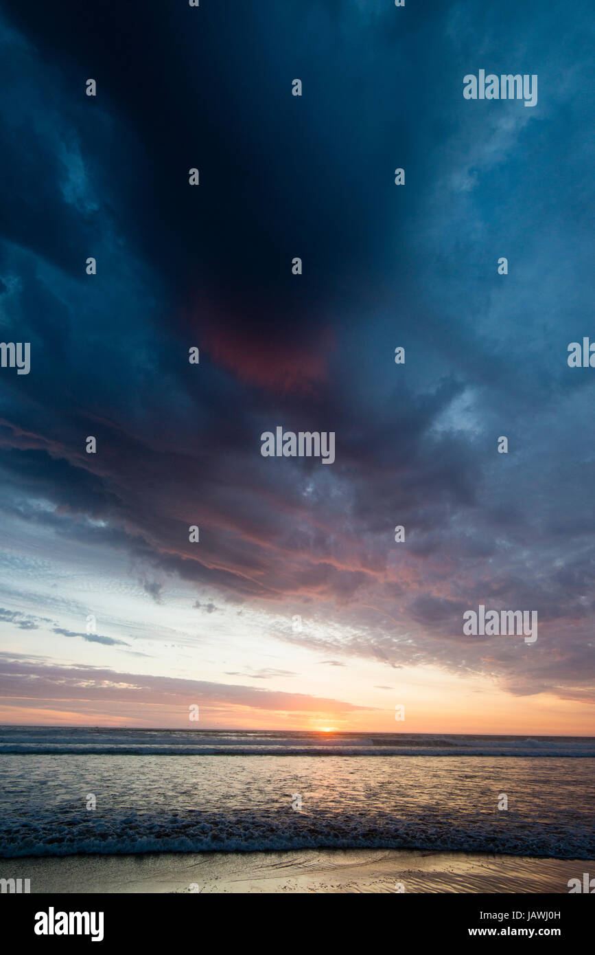 Unter ein Sturmtief schiebt eine Flut Wellen auf einen Strand bei Sonnenuntergang. Stockfoto