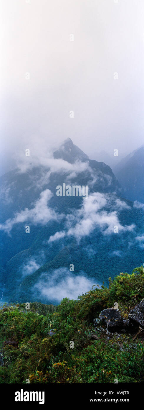 Gewitterwolken verschlingen die steilen bewaldeten Hängen und schroffen Gipfeln der Anden. Stockfoto