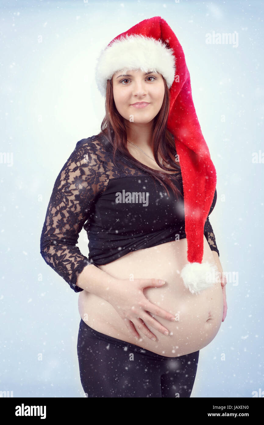 schönen lächelnden jungen Santa schwangere zärtlich hält ihren Bauch mit schneit im Hintergrund Stockfoto