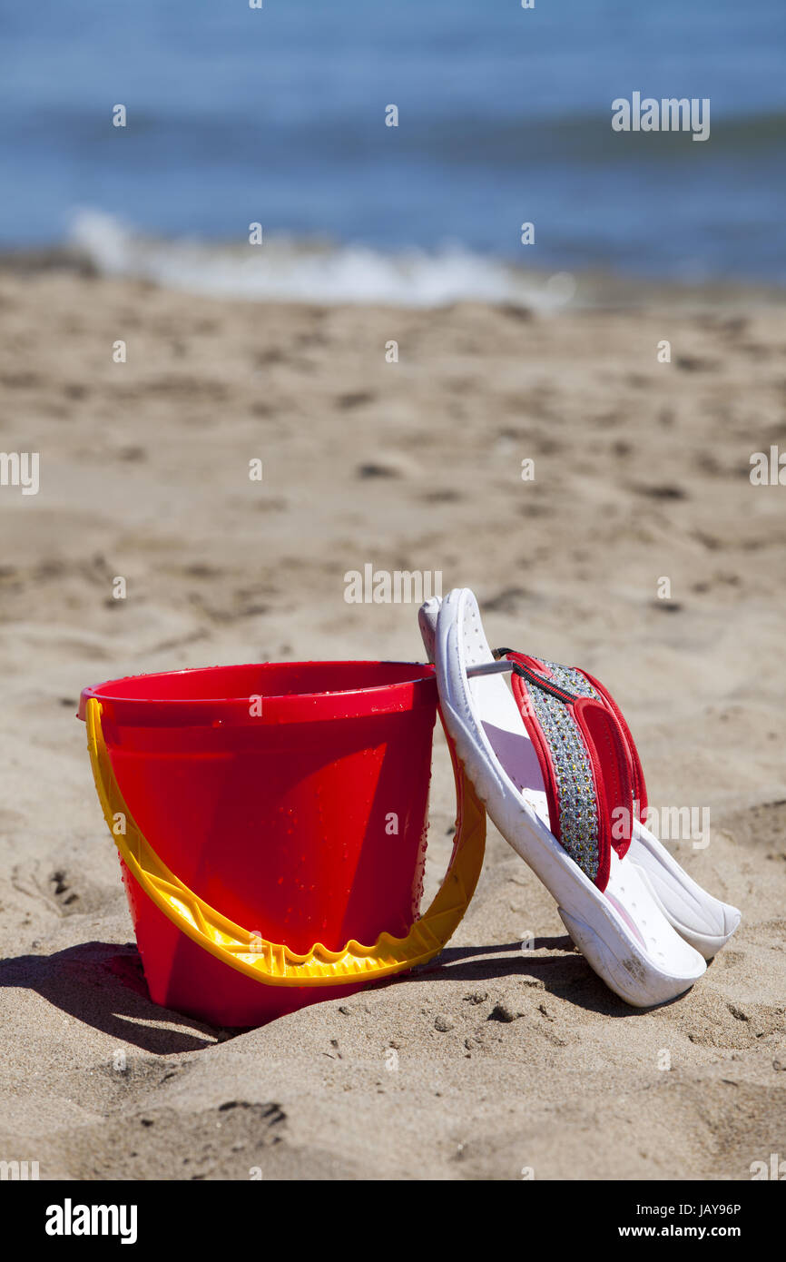 Flip Flops ein Einem Roten Eimer Angelehnt Stehen bin Strand Im Hintergrund ist Das Meer Stockfoto