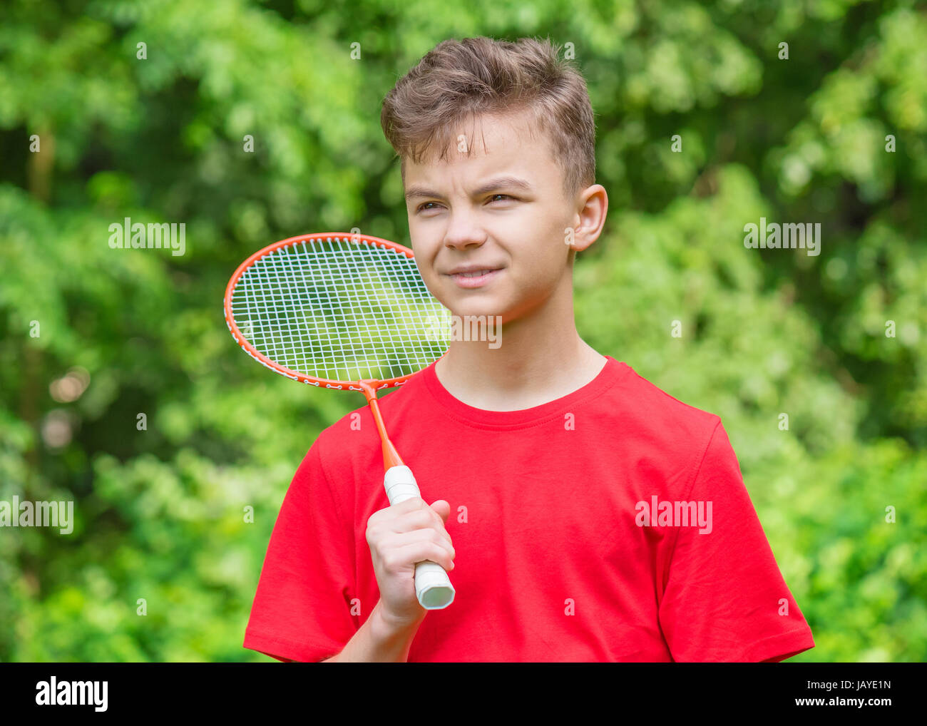 Teen junge Badminton in Wiese mit Wald im Hintergrund spielen. Kind mit Badminton Schläger in der hand. Kinder haben Spaß im Sommerpark am Tag. Stockfoto