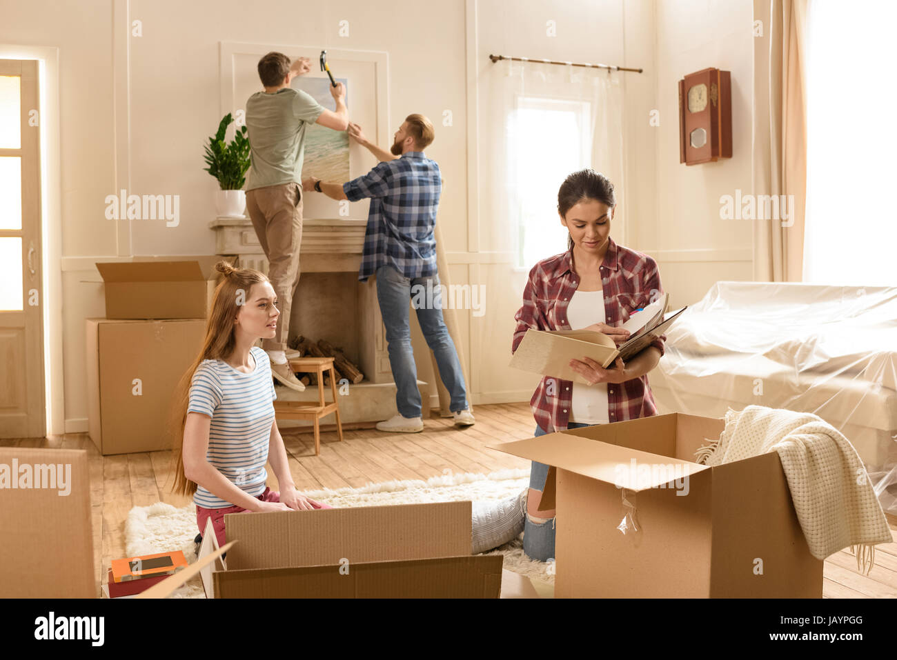 Junge Frauen, die Kisten mit Büchern während männliche Freunde hängen Bild an Wand öffnen Stockfoto