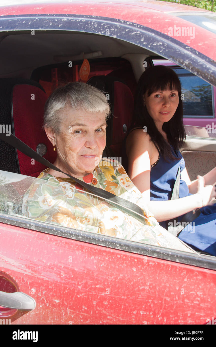 ein Enkelkind fuhr eine Großmutter auf ein Auto durch einen canicular Sonnentag Stockfoto