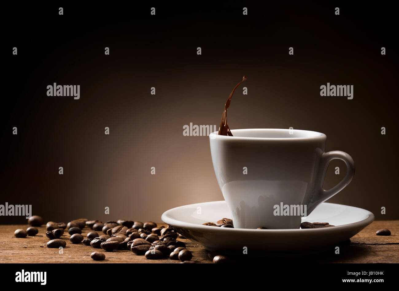 Tasse Kaffee mit Tropfen Kaffee und Kaffeebohnen auf Holztisch. Stockfoto