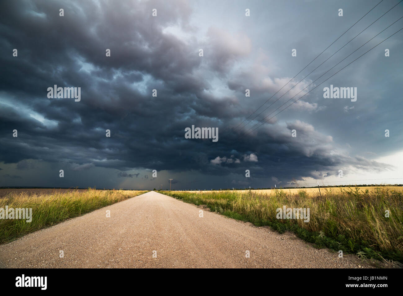 Leere Schotterstraße durch ein Feld mit dramatischen Wolken und stürmischem Himmel in Rockwood, Texas Stockfoto