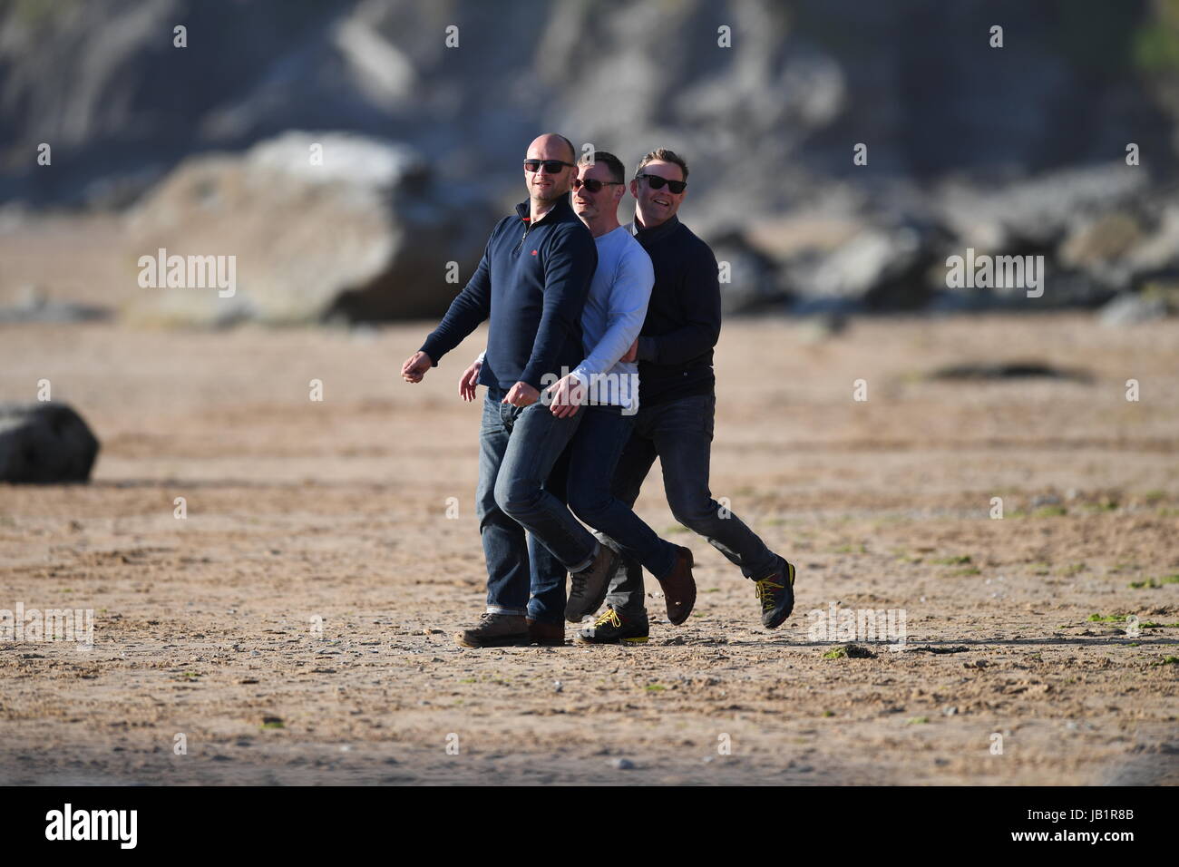 Drei Männer gehen und tanzen im Tandem am Strand Stockfoto