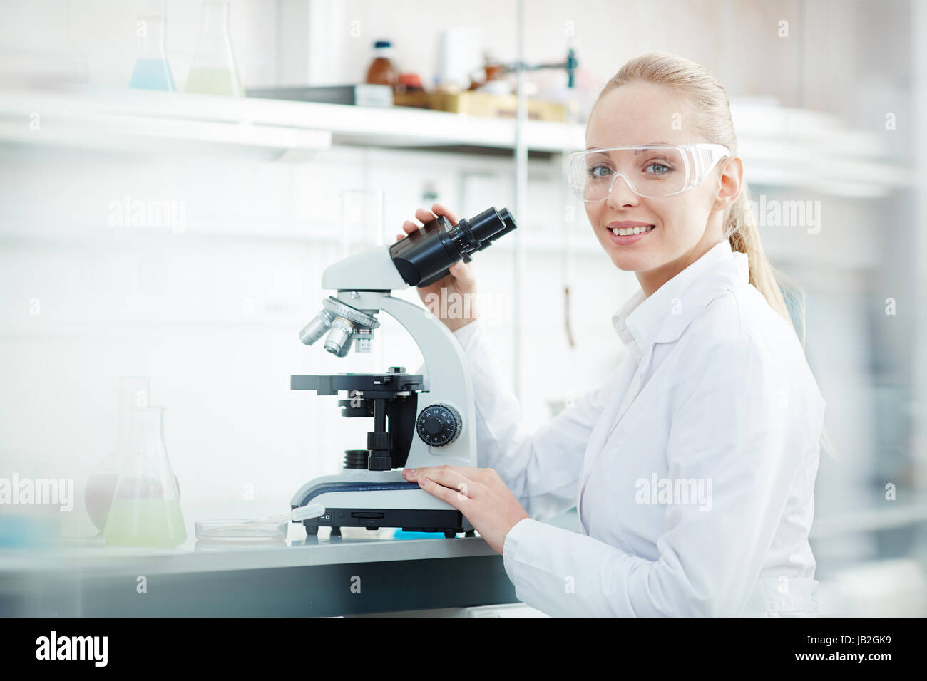 Lächelnde Frau mittels Mikroskop im Labor Stockfoto