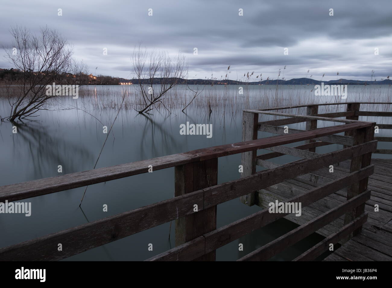 Eine Langzeitbelichtung auf Teil eines Piers an einem See mit einigen Bäumen Nachdenken über Wasser Stockfoto