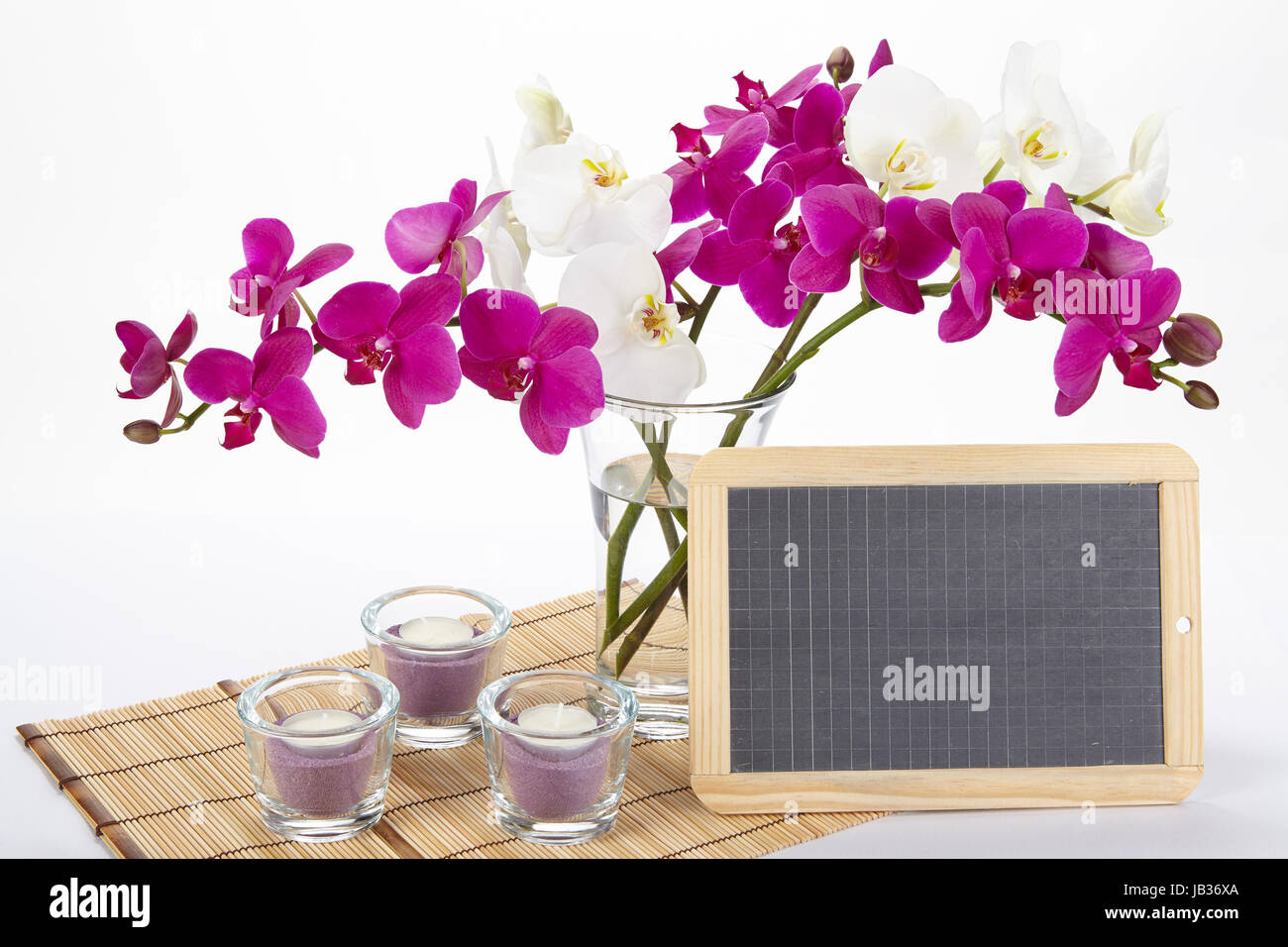 Ein Bouquet von weißen und lila Orchideen in einer Vase auf einem Tischset aus Bambus steht. Ein wenig Schiefer kann als ein freies Textfeld verwendet werden. Stockfoto