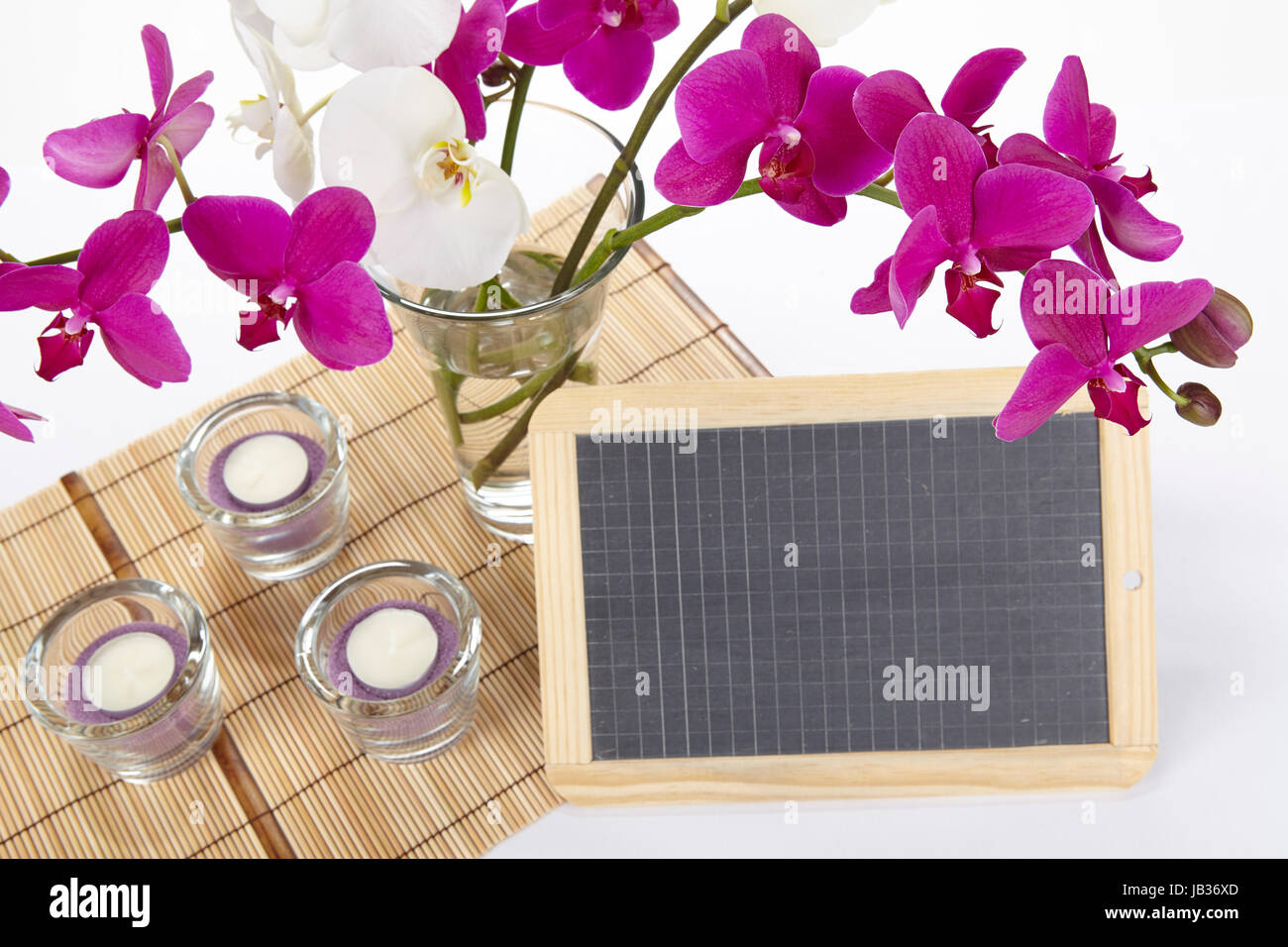 Ein Bouquet von weißen und lila Orchideen in einer Vase auf einem Tischset aus Bambus steht. Ein wenig Schiefer kann als ein freies Textfeld verwendet werden. Stockfoto