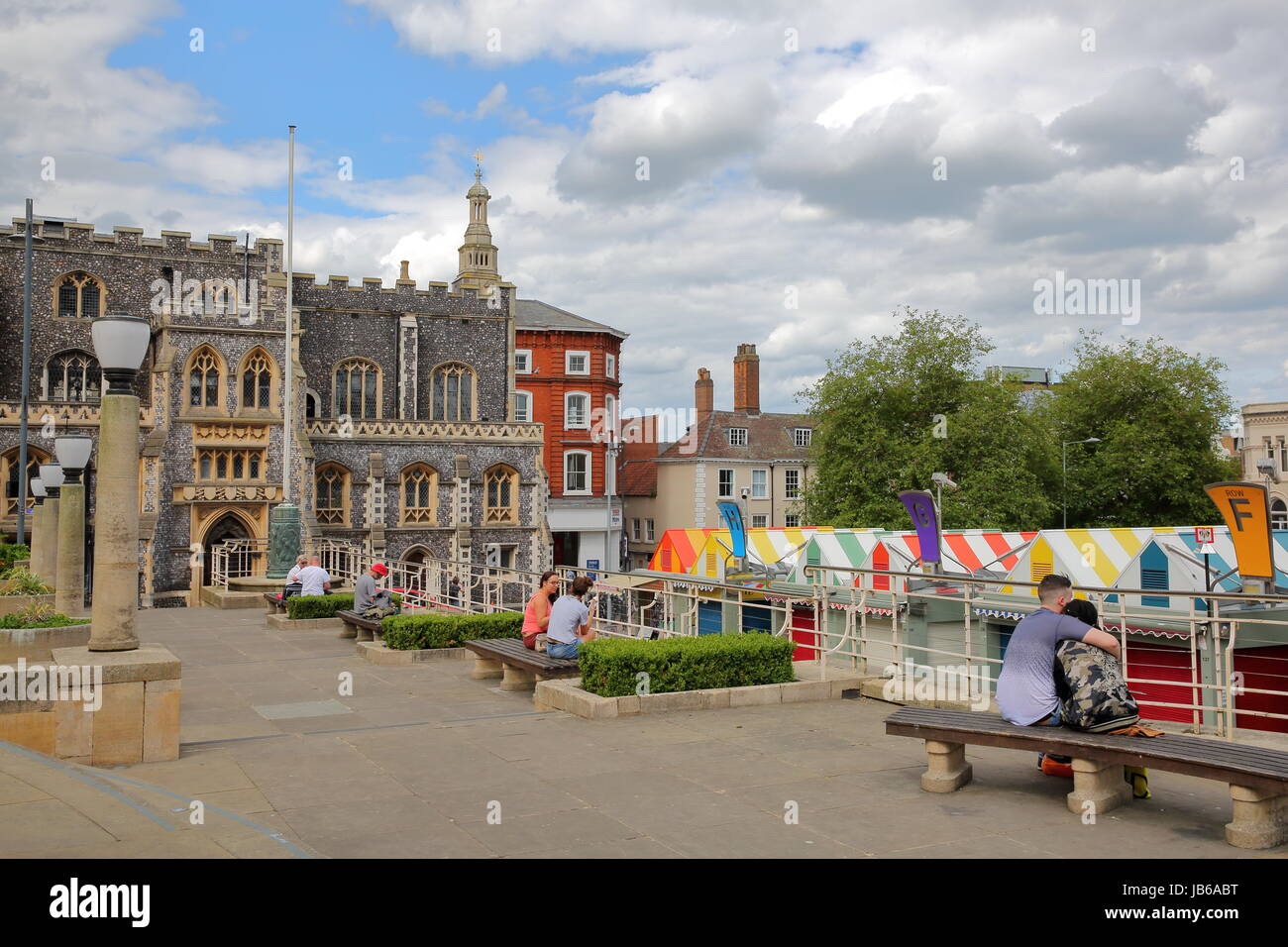 NORWICH, UK - 4. Juni 2017: Menschen entspannen bei Memorial Gardens mit Blick auf bunte Marktstände und das Rathaus im Hintergrund Stockfoto