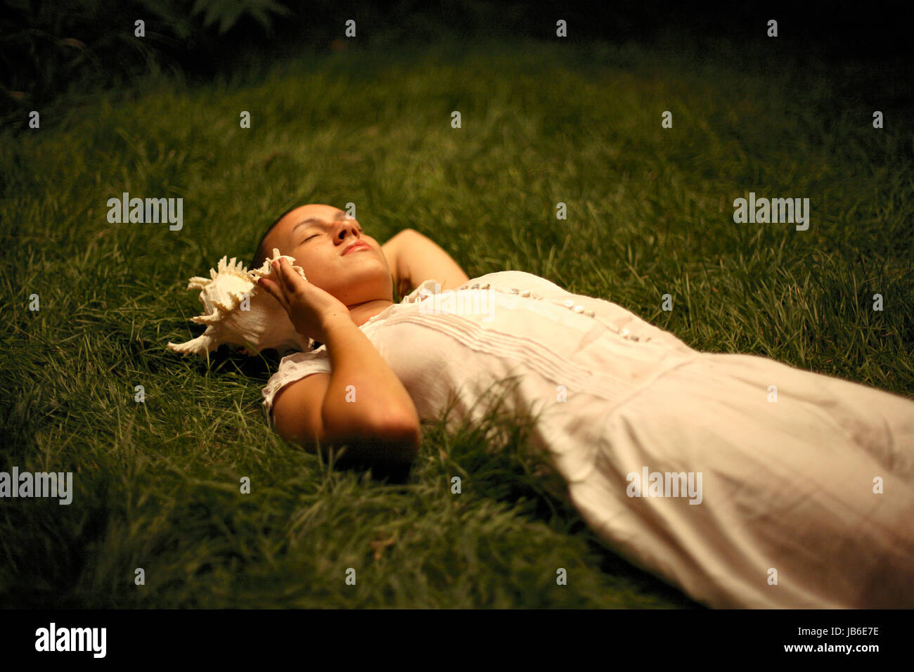 Junge unschuldige Frau auf Gras liegend und dem Muschel lauschend. 16, 17, 18, 19, 20, 21, 25, Jahre, Jahre alt Stockfoto