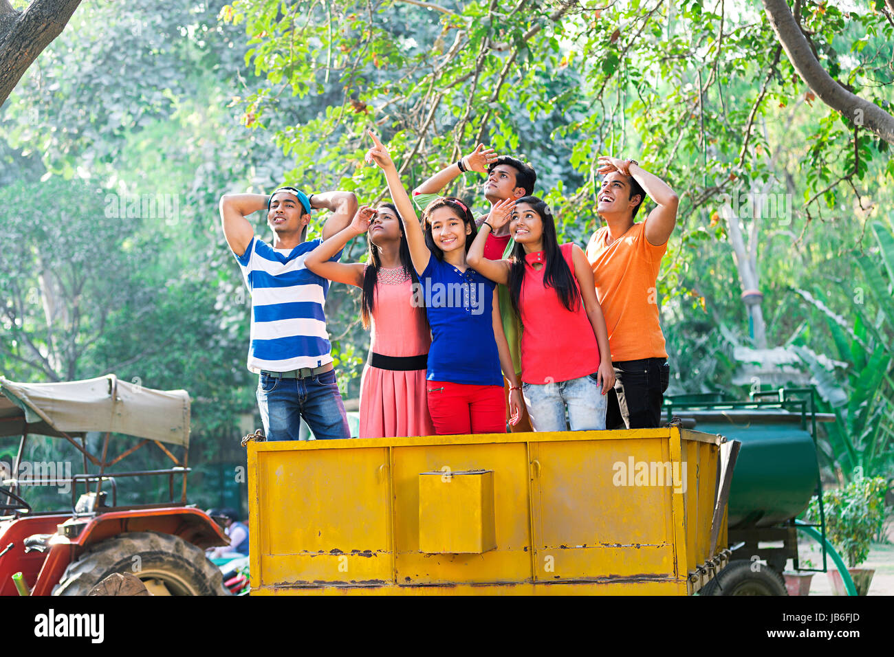 Indischer jugendlicher Mädchen und Jungen Freunde stehen auf Trolley Traktor Peekiing etwas Verweisen Stockfoto