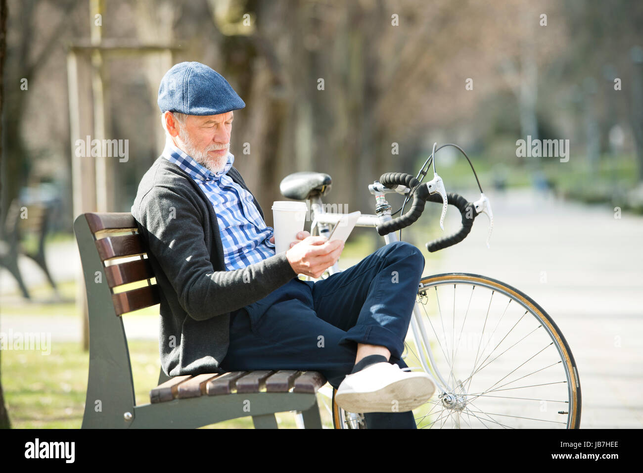 Ältere Mann auf Bank mit Fahrrad und Smartphone, SMS. Stockfoto