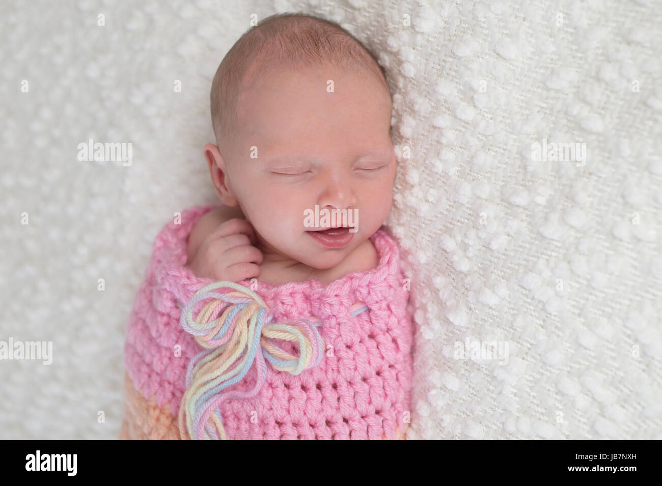 Kopfschuss von einem lächelnden drei Wochen alten neugeborenen Mädchen gebündelt in einem hellrosa, gehäkelt, kuscheln Sack. Sie liegt auf einer weißen, Bouncle Decke. Stockfoto