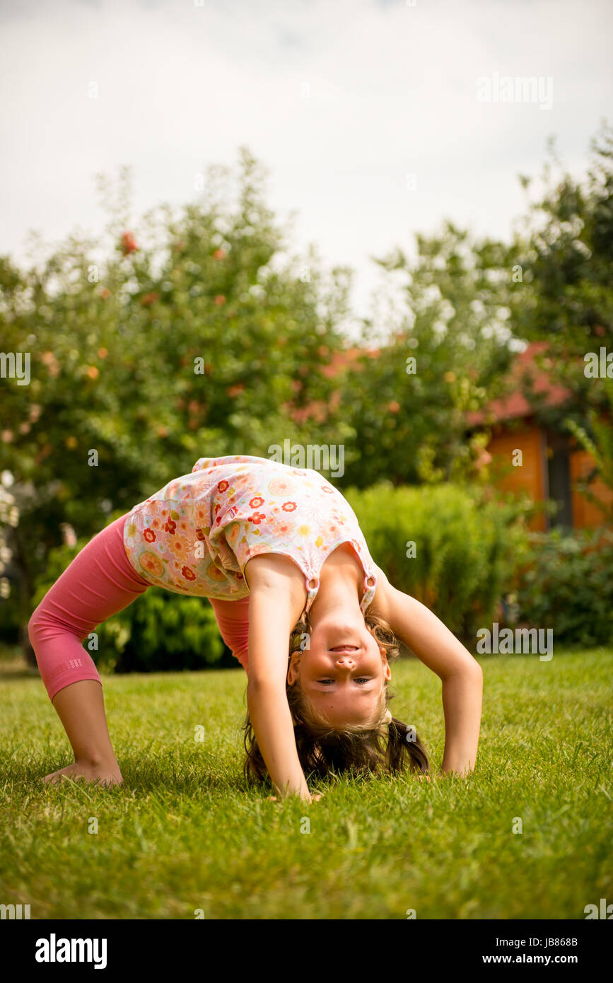 Sport auf Rasen - lächelnd kleines Kind machen Brücke im Freien im Garten Stockfoto