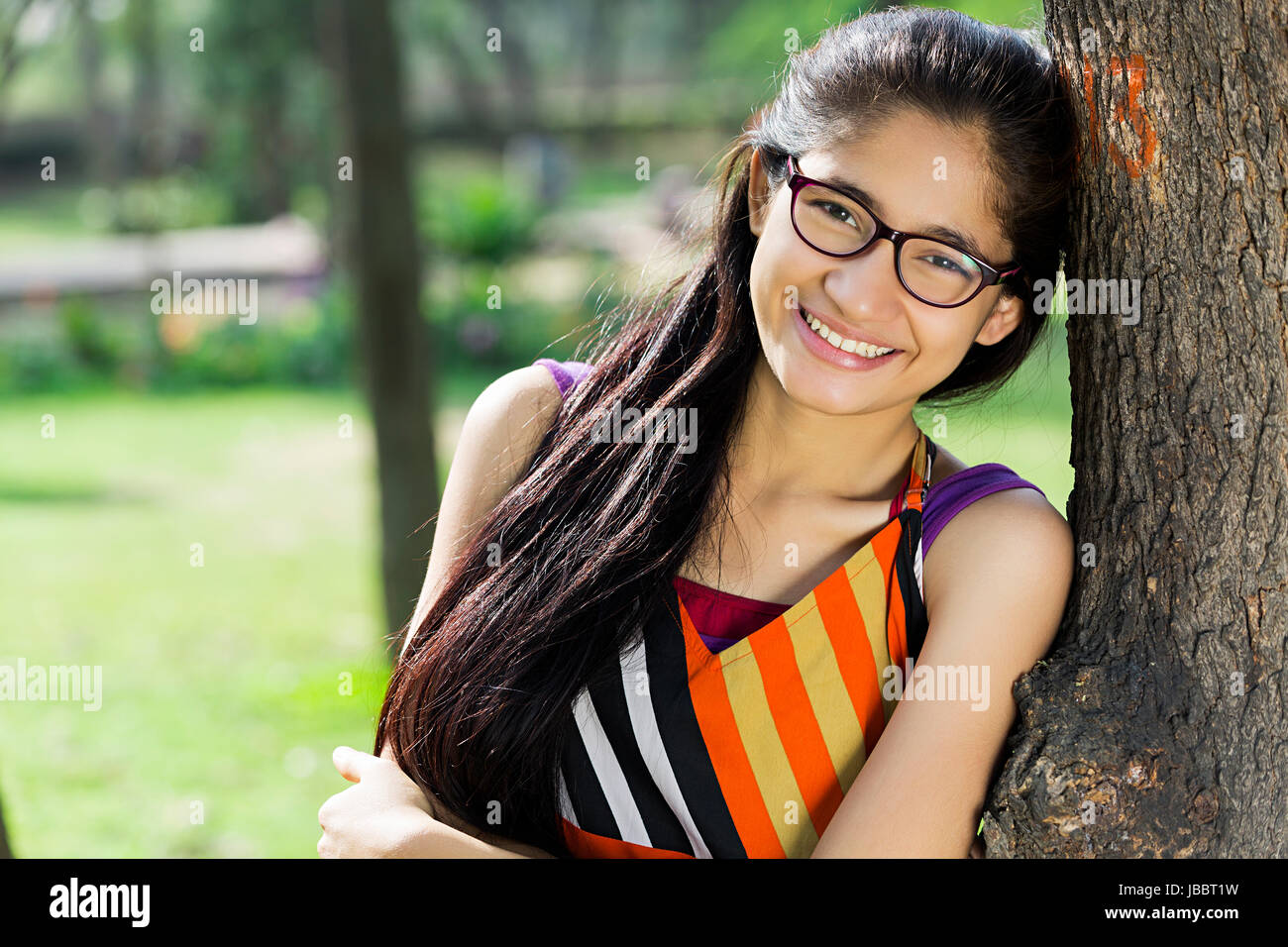 Schöne 1 indischer Jugendlicher Mädchen baum Seite stehend in Park lächelnd Stockfoto